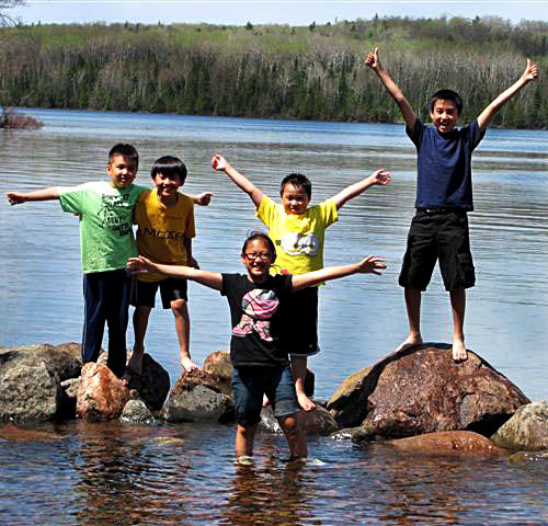 Five children standing on large rocks near the dock at Trout Lake.